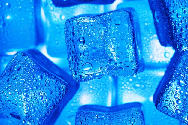 Cubos de hielo con gotas de agua esparcidas en una vista superior de fondo azul