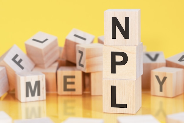 Cubos de madera con letras NPL dispuestas en una pirámide vertical, fondo amarillo, reflejo de la superficie de la mesa, concepto de negocio. npl - abreviatura de préstamos dudosos