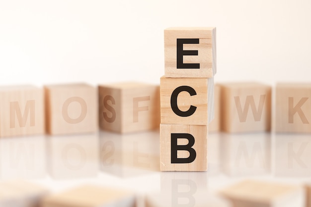 Cubos de madera con la palabra ecb dispuestos en una pirámide vertical, sobre la superficie clara hay una fila de cubos de madera con letras