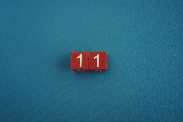 Cubos de madera Viva Magenta con el número 11 en fondo azul de primer plano vista superior Concepto de fecha u hora Números blancos 11 en cubos rojos fondo terciopelo Copiar espacio para texto o evento Cubos educativos
