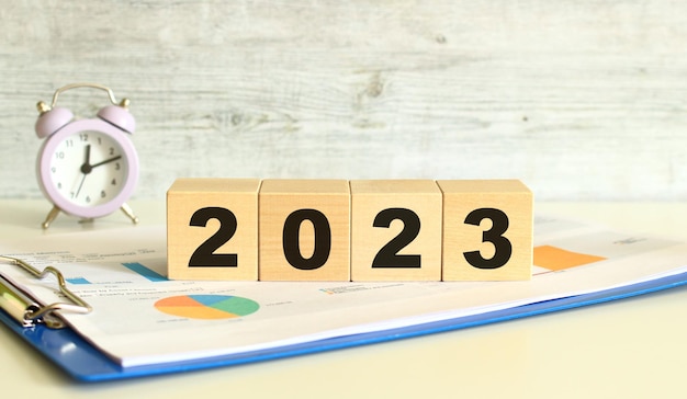 Los cubos de madera yacen en una carpeta con gráficos financieros sobre un fondo gris Los cubos forman la palabra 2023