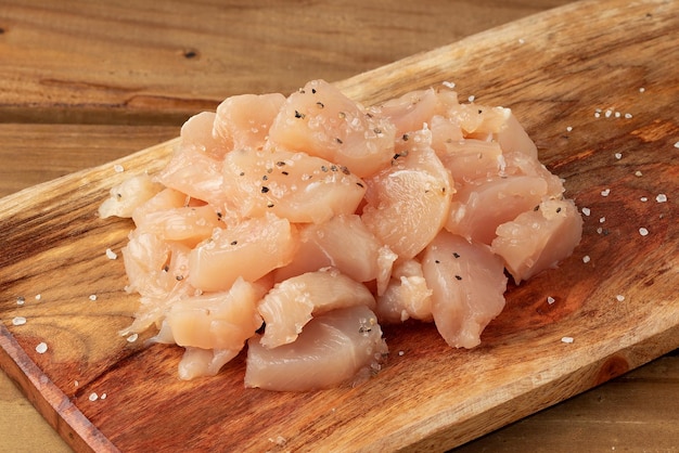 Cubos de pollo crudo con especias en tabla de cortar