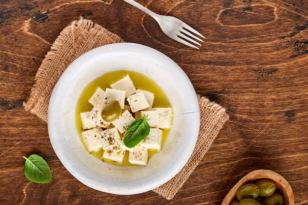 Cubos de queso feta con romero, aceitunas y aceite de oliva sobre superficie de madera.