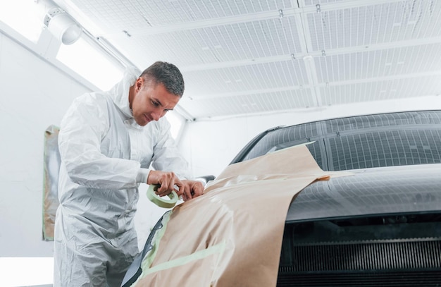 Cubriendo el coche con un paño marrón Reparador de automóviles del Cáucaso en uniforme trabaja en el garaje