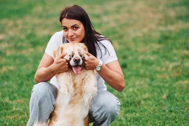 Foto cubriendo los ojos con las patas una mujer con un lindo perrito retriever dorado está en el campo verde