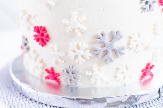 Cubriendo un pastel redondo alto con glaseado de crema de mantequilla italiana blanca y decorando con copos de nieve de fondant.