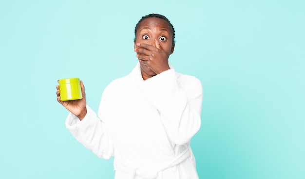 Cubrirse la boca con las manos con una bata de baño sorprendida y una mascarilla para el cabello