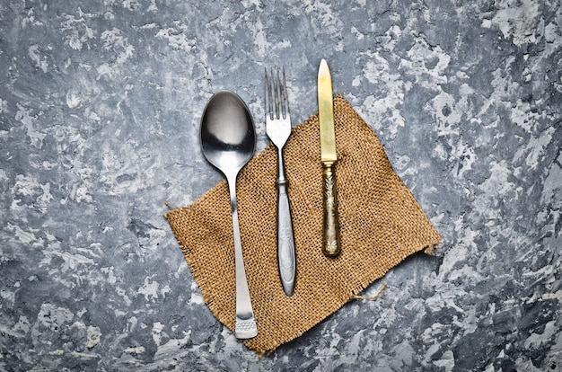 Cuchara antigua, tenedor, cuchillo en una servilleta se encuentran en una mesa de hormigón gris. Vista superior.