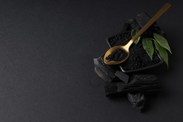 Cuchara de carbón en polvo de carbón y hojas sobre fondo negro