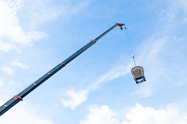 Cuchara de cemento o hormigón colgando de un cable en el sitio de construcción con fondo de cielo azul