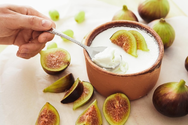 Cuchara y delicioso yogur griego natural en cuenco de barro con higos