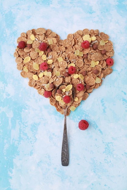 Cuchara y forma de corazón de copos de maíz muesli saludable en azul.