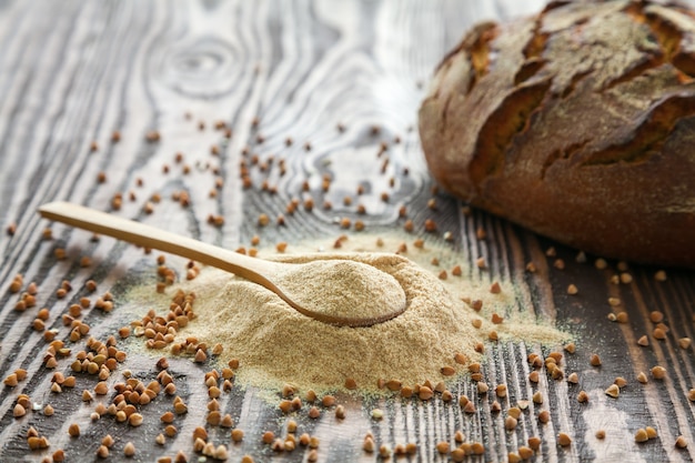 Cuchara con harina de trigo sarraceno y un pan sobre un fondo de madera. Harina alternativa. Alimentación sana y sin gluten.