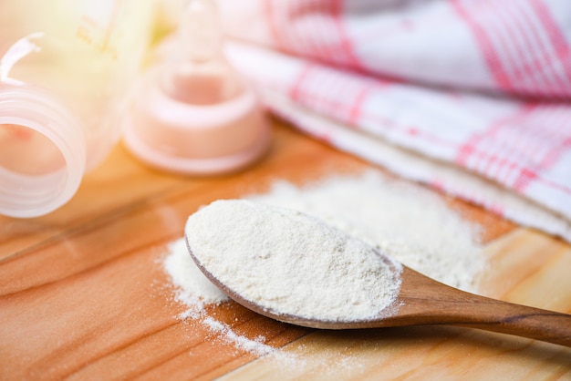 Cuchara de leche en polvo con biberón de leche en mesa de madera