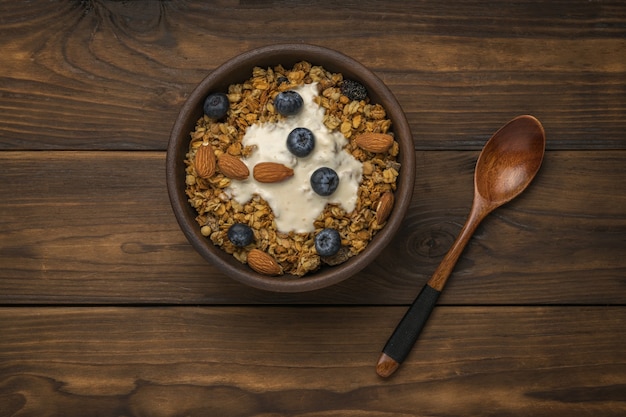 Cuchara de madera y cuenco con muesli y yogur en una mesa de madera. Endecha plana.