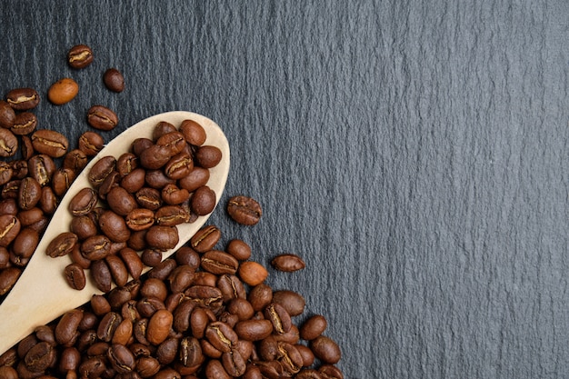 Una cuchara de madera con granos de café sobre un fondo de pizarra