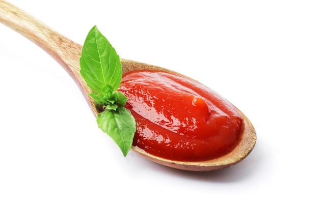 Foto cuchara de madera llena de salsa de tomate con albahaca fresca aislada de fondo blanco