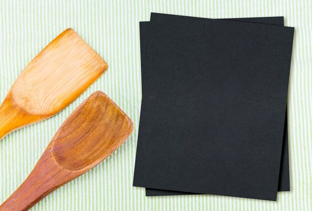 Cuchara de madera en mantel verde con papel de menú negro en blanco