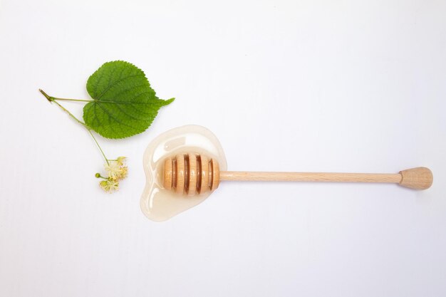 Cuchara de madera de miel y miel de tilo y flores de tilo sobre un fondo blanco.