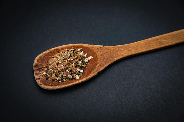 Foto cuchara de madera con sal y especias sobre un fondo oscuro