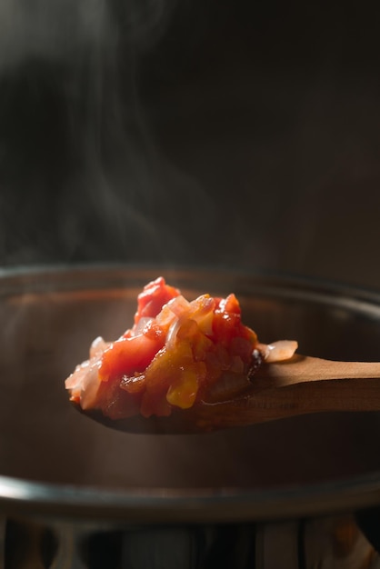 Cuchara de madera con tomate y calabaza sobre la sartén.