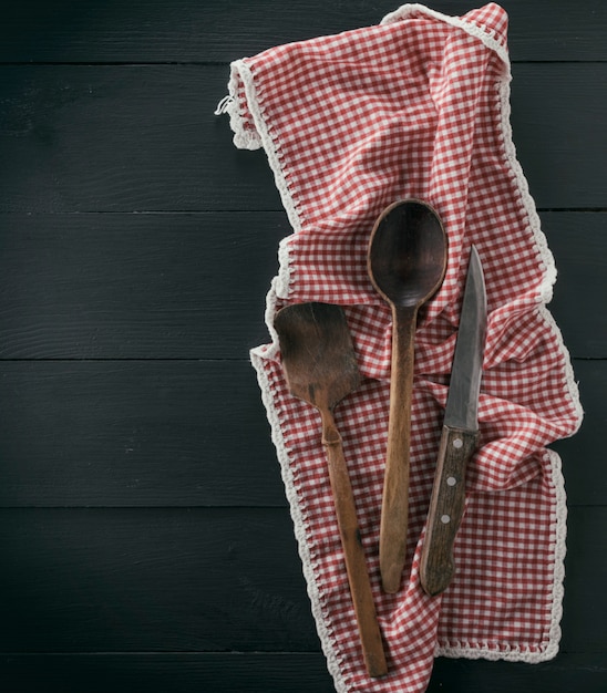 Cuchara de madera vieja, escápula y cuchillo en una toalla roja textil
