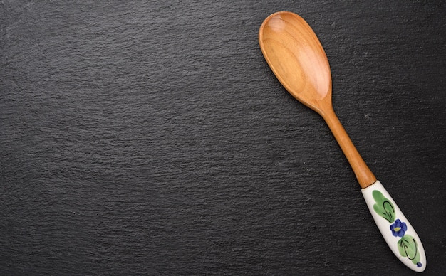 Cuchara de madera vintage vacía con mango de cerámica sobre fondo negro, vista superior