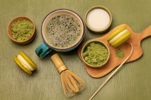 Cuchara de medición polvo de matcha verde y galletas de macarrón en tabla de madera Leche en cuenco Té de matcha en taza