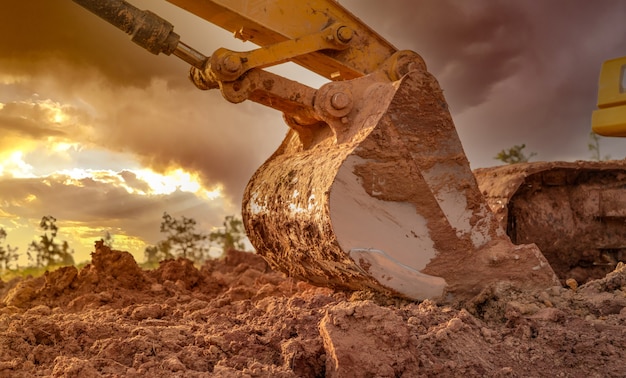 Cuchara de metal para la suciedad de la retroexcavadora después de excavar el suelo. Retroexcavadora estacionada en tierras agrícolas en el cielo del atardecer. Excavadora de cadenas. Máquina de movimiento de tierras en el sitio de construcción al anochecer. Vehículo de excavación.