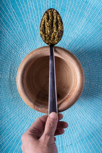 Foto cuchara de pesto en un cuenco de madera sobre un fondo azul claro