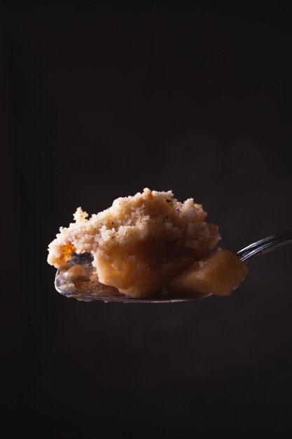 Cuchara que muestra un trozo de manzana casera desmenuzada con poca luz Foto de comida oscura con espacio de copia