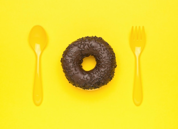 Cuchara y tenedor amarillo de donut de chocolate fresco sobre un fondo amarillo El concepto mínimo de horneado popular