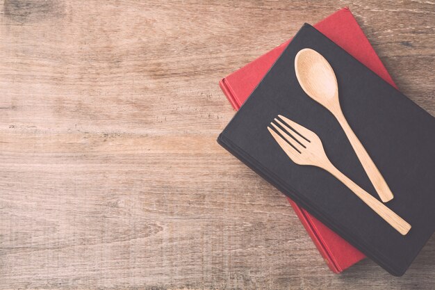 Cuchara, tenedor y libro de la visión superior en fondo de madera del tablón. Comer el concepto de conocimiento