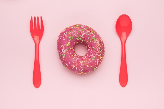 Cuchara y tenedor rojo y donut rojo sobre fondo rosa El concepto mínimo de horneado popular