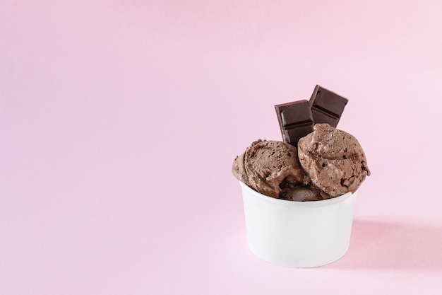 Cucharadas de helado de chocolate en una taza de papel sobre fondo rosa Helado para llevar