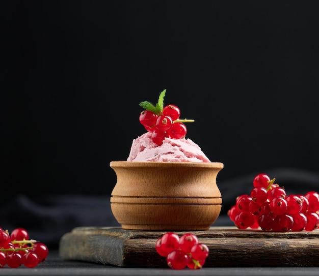 Cucharadas rosas de paletas con grosellas rojas sobre una mesa negra Helado