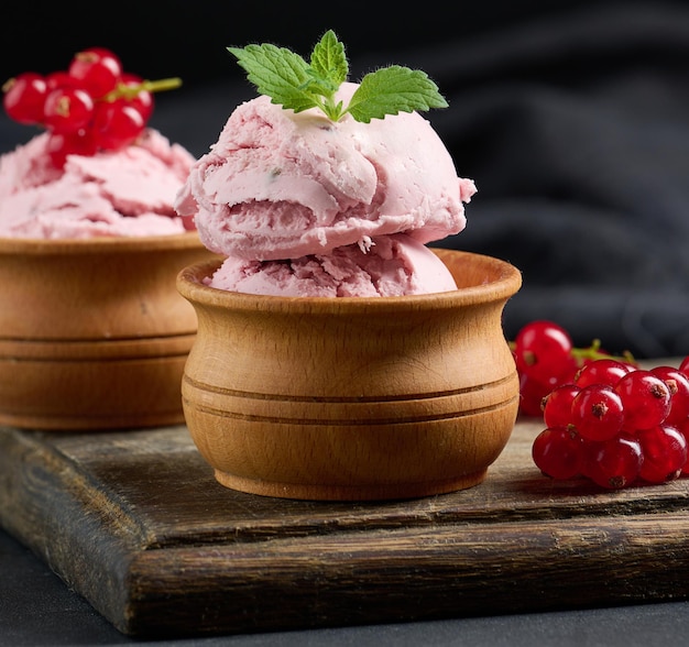 Cucharadas rosas de paletas con grosellas rojas sobre una mesa negra Helado