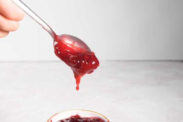 Foto cucharadita con mermelada de cereza roja cayendo sobre una mesa de piedra gris