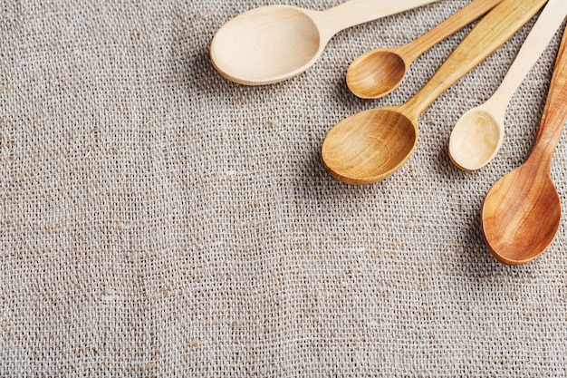 Cucharas artesanales hechas de diferentes tipos de madera se encuentran en una fila sobre una tela de arpillera de cáñamo