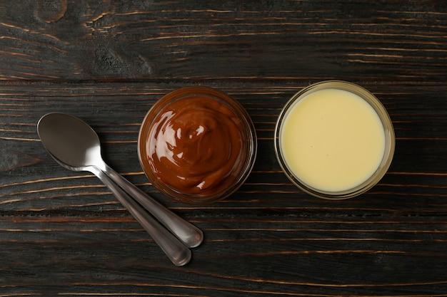 Cucharas y cuencos con leche condensada sobre fondo de madera