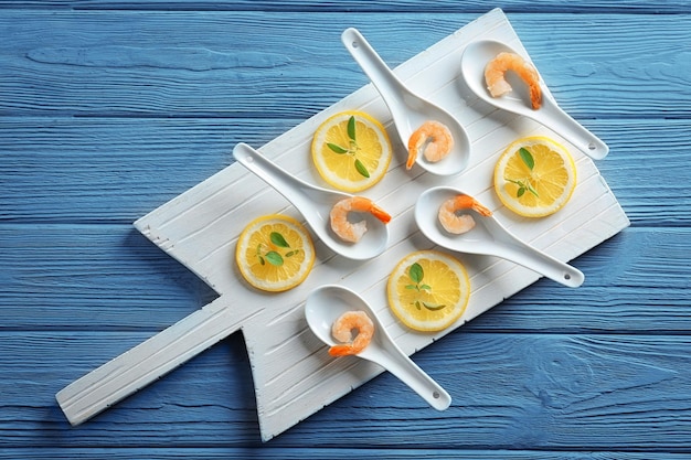 Cucharas con deliciosos camarones y limón sobre tabla de madera.