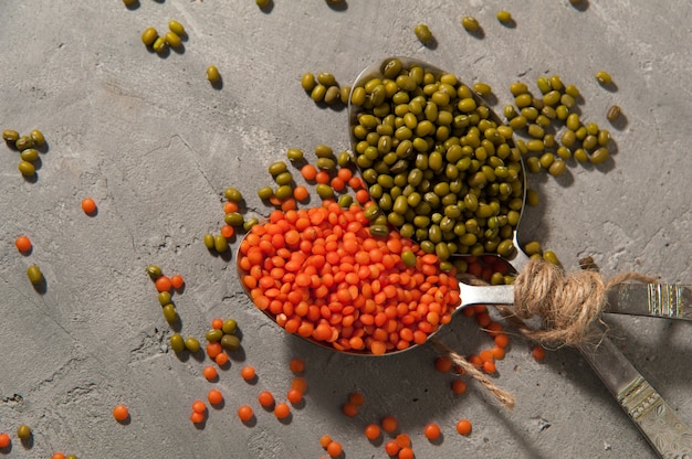 Cucharas con lentejas rojas y frijol mungo en una superficie gris - superalimento, comida sana.