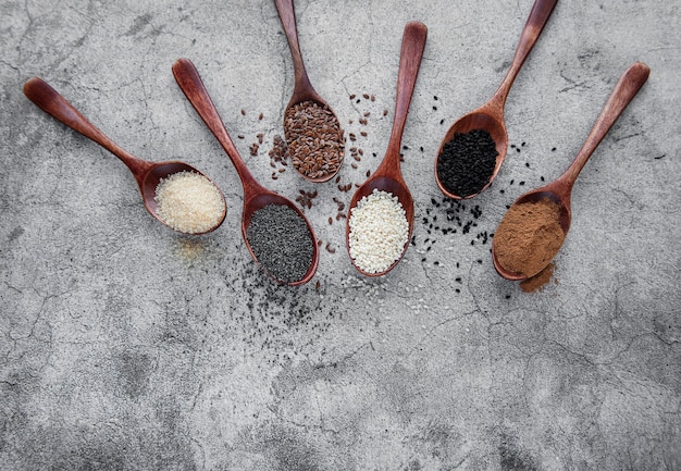 Cucharas de madera con diversas semillas y especias saludables sobre fondo de hormigón gris