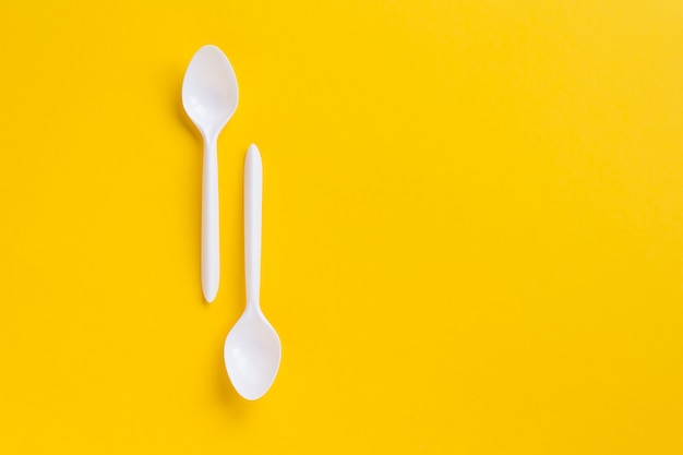 Foto cucharas de plástico blanco sobre fondo amarillo. flatlay