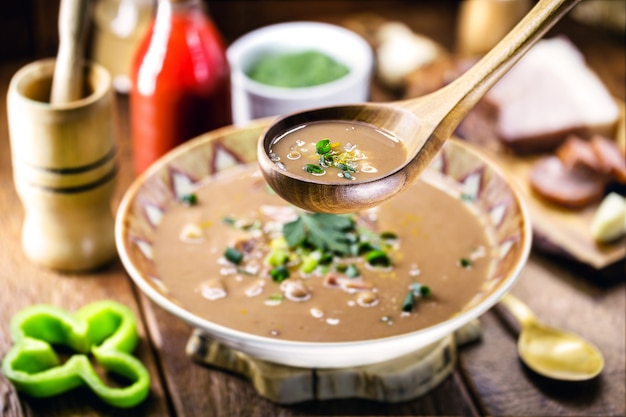 Cucharón de crema o sopa de frijoles con ingredientes al fondo, pepperoni, tocino y verduras