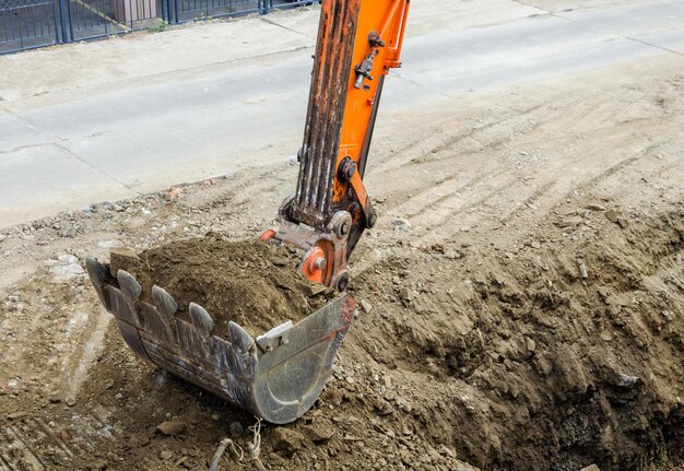 El cucharón de la excavadora cava una zanja en el suelo.