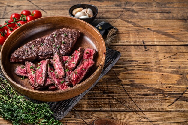 Cuchilla superior en rodajas a la parrilla o filete de carne de res de Denver en una placa de madera con hierbas.