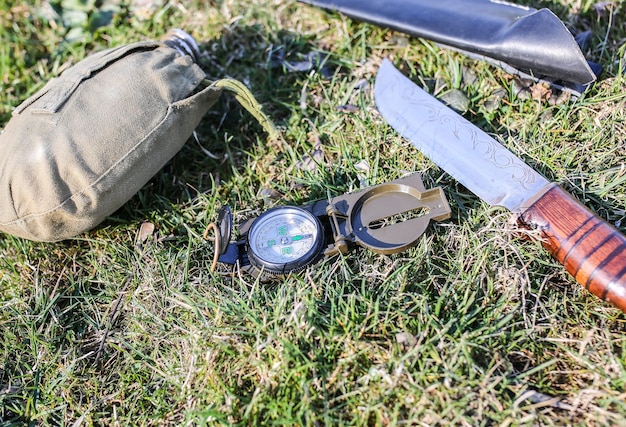 Cuchillo, brújula y matraz tirado en la hierba. Cosas turísticas para hacer senderismo en la naturaleza. Estilo vintage antiguo.