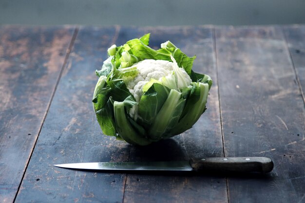 Foto cuchillo, coliflor con hojas verdes se encuentran en una mesa de madera