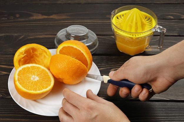 El cuchillo cortado a mano hace mitades de naranjas para luego exprimir jugo fresco en el exprimidor